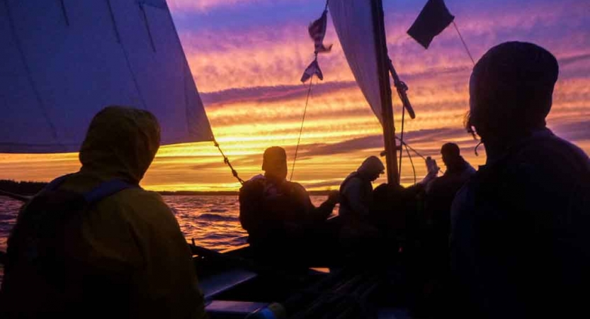 the silhouette of a group of people on a sailboat at sunset